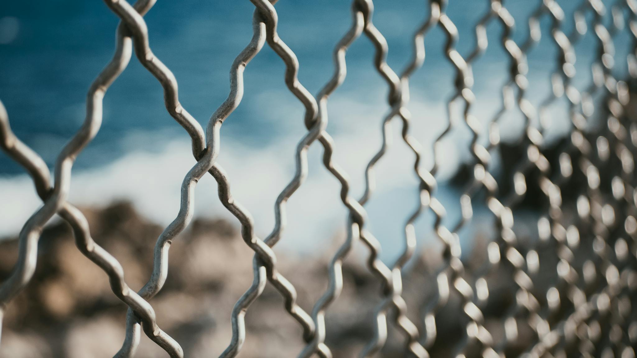 Selective focus on a chain link fence with ocean background, emphasizing depth.